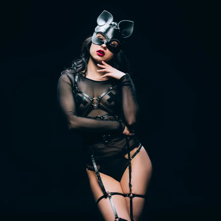 Mujer con máscara de cuero y arnés en un look sensual y atrevido sobre fondo oscuro.