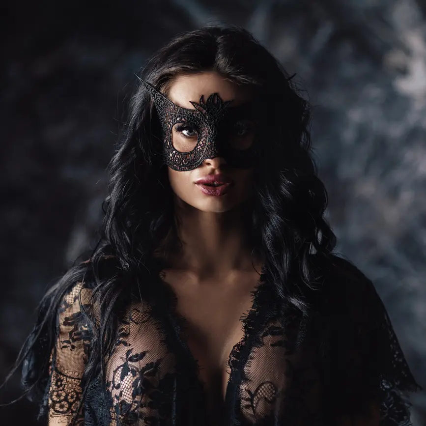 Mujer con máscara negra decorativa y lencería de encaje, con mirada intensa y fondo oscuro artístico.