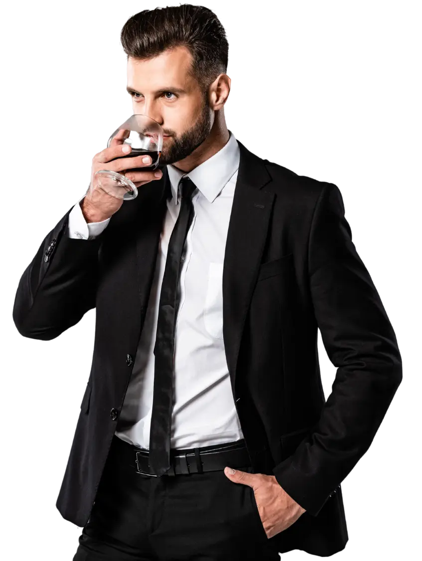 Hombre con barba bien cuidada, vistiendo un traje negro con camisa blanca y corbata, sosteniendo una copa de vino tinto mientras mira con confianza.